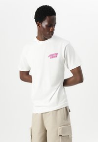 White cotton t-shirt featuring a pink "SANTA CRUZ" logo on the left chest, crew neck design, and short sleeves, paired with beige cargo shorts.
