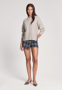 Jasbeżowy sweter dzianinowy z prążkowanym wykończeniem, w zestawie z granatowymi szortami w kratę. Szorty mają luźny krój i boczne rozcięcia. Brązowe buty na obcasie.