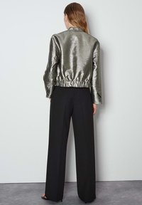 Metalen zilveren bomberjack met eenGathered tailleband, gecombineerd met zwarte wijde broek. De texturen zijn strak en reflecterend.