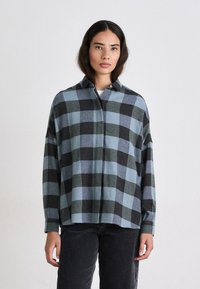 Camicia flanella oversize con un motivo a quadri nero e blu, colletto con bottoni e maniche lunghe; texture morbida e vestibilità rilassata.