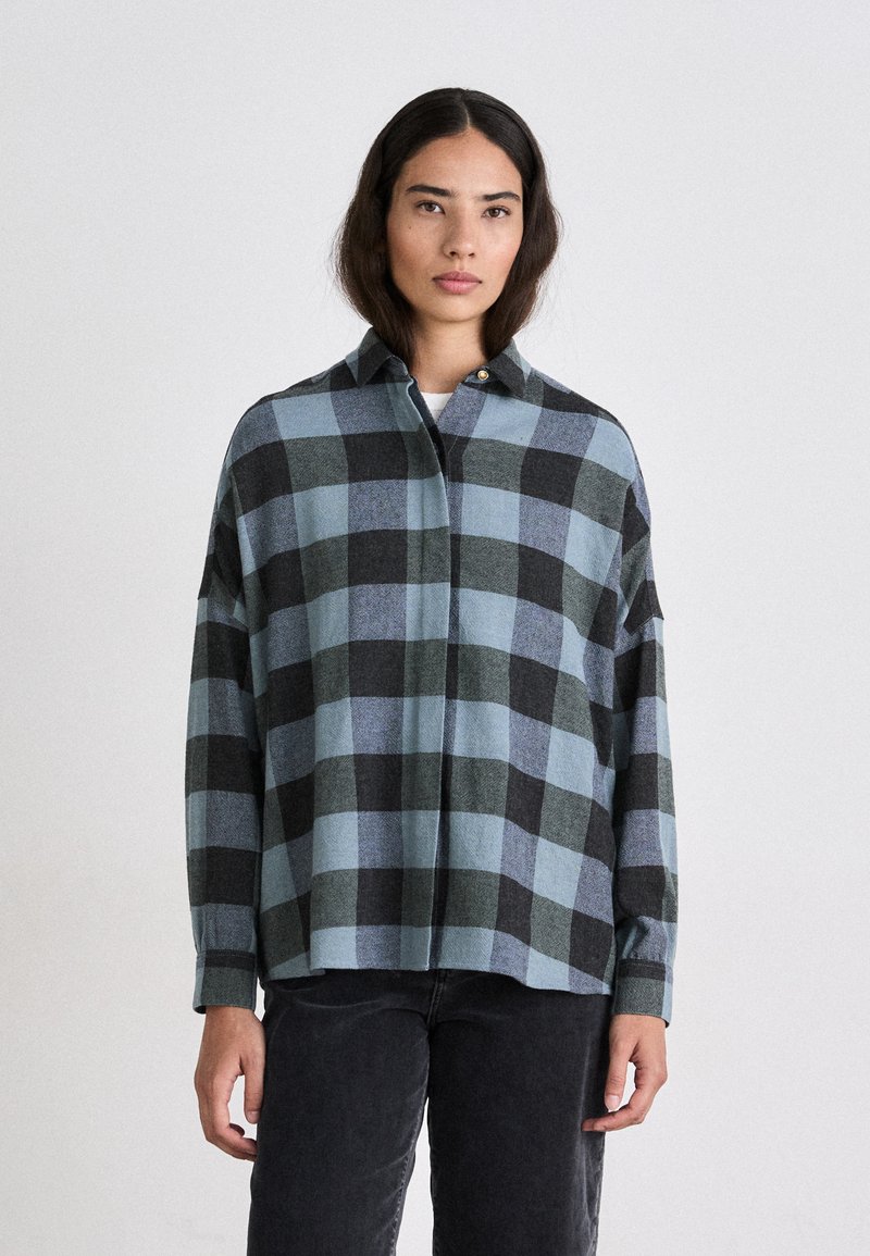 Camicia flanella oversize con un motivo a quadri nero e blu, colletto con bottoni e maniche lunghe; texture morbida e vestibilità rilassata.