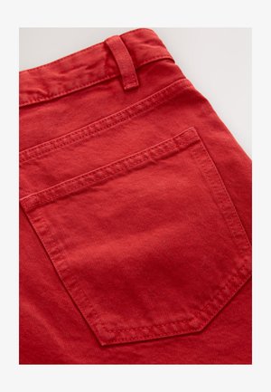 Tessuto di velluto a coste rosso con trama visibile, caratterizzato da una tasca posteriore a forma esagonale e cuciture a contrasto vicino alla vita.