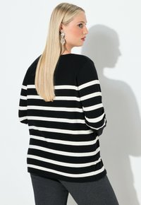 Sweter w czarno-białe paski z długimi rękawami, okrągłym dekoltem i luźnym krojem. Stylizowany z szarymi legginsami, podkreślającymi czyste linie.