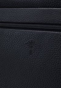 Borsa nera in pelle con texture, dotata di chiusura con cerniera e un sottile emblema in rilievo, che mette in risalto i dettagli del materiale e del design.