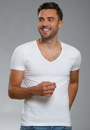 Witte T-shirt met korte mouwen en V-hals, gemaakt van zachte, gladde stof. Heeft een getailleerde snit en een casual ontwerp. Gemaakt om te dragen met blauwe jeans.