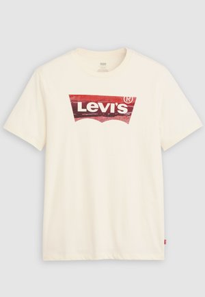 Tricou alb cu mâneci scurte, cu un logo Levi's roșu uzat în centru și o etichetă mică roșie Levi's pe cusătura laterală.