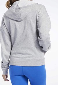 Felpa grigia con cappuccio bordato di bianco, caratterizzata da una vestibilità comoda e polsini a coste. Abbinata a leggings blu, che presentano una texture liscia.