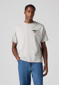 T-shirt en coton gris à manches courtes, présentant un graphique de plante verte et un logo Levi's rouge sur la poitrine gauche. Coupe décontractée, col rond.
