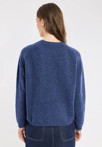 Pull en tricot bleu avec une finition texturée, des manches larges et un ourlet légèrement court. Le dos présente un col rond classique.