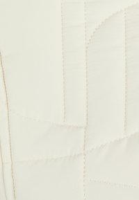 Gequilte beddengoed in crèmekleurige stof met zichtbare stiksels, met geometrische vormen en een gladde textuur.