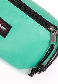 Pocchetto turchese realizzato in tessuto texture con cerniera nera e linguette; dotato di un'etichetta con il logo Eastpak. Forma rettangolare compatta.