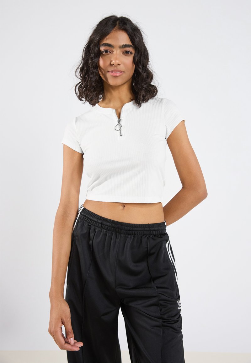 Fehér, bordázott, rövid ujjú crop top elöl cipzárral, fekete, laza szabású sportnadrággal, illetve oldalsó csíkokkal párosítva.