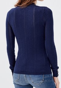 Tmavě modrý pletený svetr s vertikálním žebrováním, dlouhými rukávy a manžetami na knoflíky. Mírně přiléhavý v pase pro štíhlý vzhled.