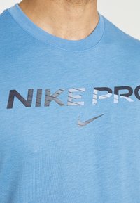 Camiseta Nike Pro azul claro con cuello redondo y un gran gráfico "NIKE PRO" en negro y multi-texturizado, además de un pequeño logo del swoosh de Nike.