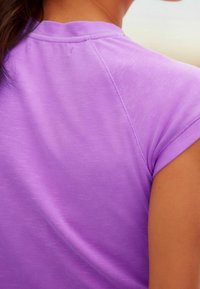 Close-up of a person wearing a short-sleeve lavender shirt, showing shoulder and upper back with visible seam details.