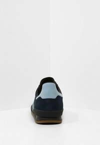 Mörkblå mockasportskor med en ljusblå hälkappa och svarta detaljer. Har en strukturerad design och en gummisula för grepp.