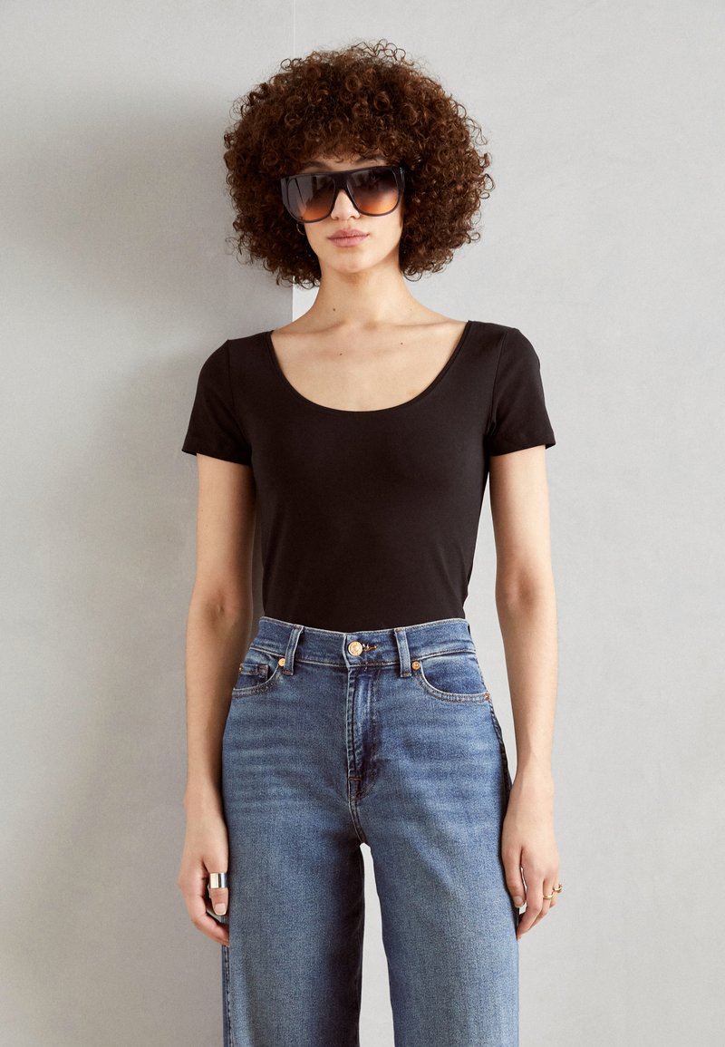 Haut noir à manches courtes avec un col rond, associé à un jean large taille haute bleu clair. Le modèle porte de grandes lunettes de soleil foncées.