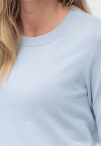Světlomodrý svetr s kulatým výstřihem, měkkou texturou a žebrovanými manžetami. Materiál působí hladce s jemným leskem.