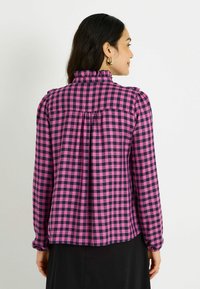 Camisa de manga larga en un patrón de cuadros rosa y marino, con un cuello con volantes, detalle de gather en la parte posterior y puños elásticos.
