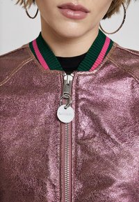Metaliczna różowa bomberka z srebrnym suwakiem, zielono-różowym, prążkowanym kołnierzem oraz okrągłą metką z logo. Fakturowana powierzchnia.