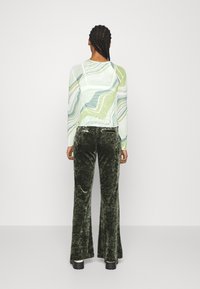 Camisola de manga longa com um padrão em espiral nas cores verde, azul e branco; combinada com calças boca de sino em veludo texturizado de cor verde escura e sapatos pretos robustos.