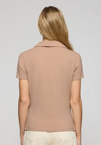 Koszulka polo z krótkim rękawem w jasnobrązowym kolorze, wykonana z miękkiego materiału, z klasycznym kołnierzykiem i dopasowanym fasonem. Gładka faktura bez wzorów.