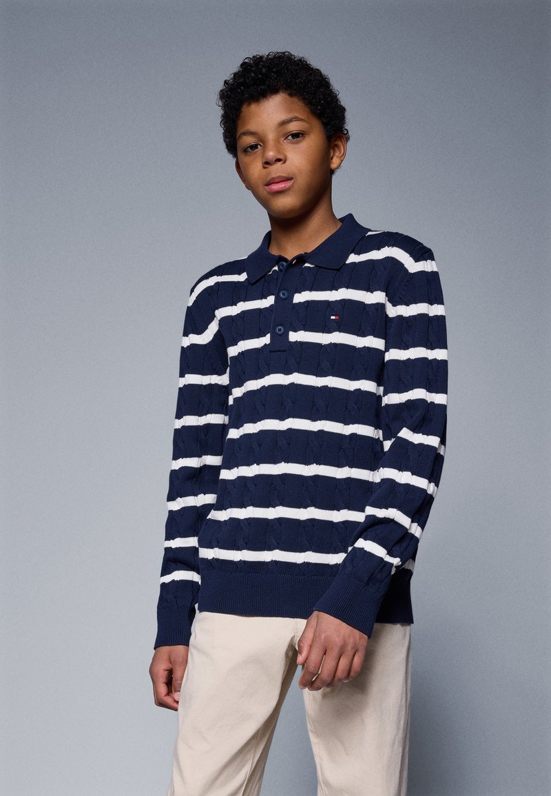 Marineblå og hvit stripete langermet polo med teksturert mønster, knappestolpe med tre knapper, ribbet mansjetter og hem. Lys beige bukser.