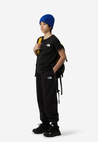 Μαύρο βαμβακερό T-shirt και φόρμες με λογότυπα, συνδυασμένα με μπλε πλεκτό σκουφάκι και κίτρινο σακίδιο πλάτης, που ολοκληρώνουν την casual εμφάνιση.