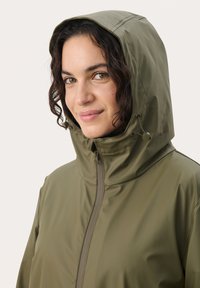 Jachetă impermeabilă verde, cu glugă, dotată cu fermoar frontal, șnur reglabil și o textură netedă, lucioasă.