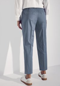 Jasnoniebieskie spodnie o prostym kroju, z dwoma tylnymi kieszeniami i subtelnymi zagnieceniami, połączone z białymi tenisówkami.