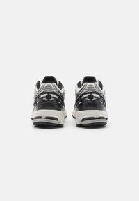 Schwarze und graue Sportschuhe mit einem strukturierten Design, ausgestattet mit einer gepolsterten Sohle und kontrastierenden Materialien. Die Ansicht von hinten zeigt die gestapelte Konstruktion.