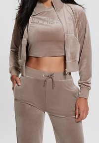 Brown velours cropped jacket met een ritssluiting aan de voorkant en zakken, gedragen met bijpassende hoge taillebroek met een verstelbaar trekkoord.