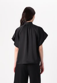 Blusa nera in satin con maniche corte a scallop, collo alto e dettaglio arricciato nella parte posteriore. Il tessuto ha una consistenza liscia e lucida.
