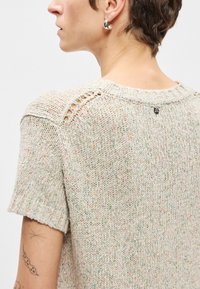 Ανοιχτό γκρι πουλόβερ πλεκτό με κοντά μανίκια, που διαθέτει υφή πλεξίματος, διακριτά πολυχρωματικά φιτίλια και ανοιχτή βελονιά στους ώμους.