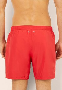 Bañador rojo hecho de una tela ligera con una cinturilla elástica, que presenta dos ojales en la parte posterior y un acabado suave y plano.