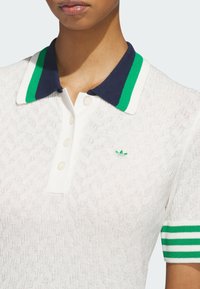 Hvit poloskjorte i teksturert strikket stoff, med en marineblå krage med grønne striper og tre knapper. Liten grønn logo på brystet.