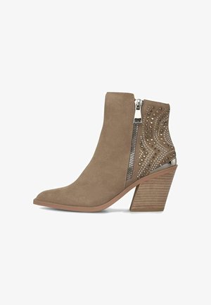 Anfibio alla caviglia in suede marrone chiaro con punta affilata, cerniera metallicain e borchie decorative con motivi ondulati sul lato. Tacco in legno spesso.