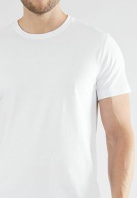 Weißes Baumwoll-T-Shirt mit Rundhalsausschnitt, kurzen Ärmeln und glatter Textur. Schmiegt sich eng an den Körper an und präsentiert ein sauberes und einfaches Design.