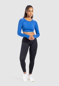 Blaues Crop-Top mit langen Ärmeln und figurbetontem Design, kombiniert mit hoch taillierten schwarzen Leggings und weißen Sneakern, aus glattem, elastischem Stoff.