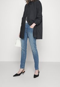 Černá oversize košile s balónovými rukávy, světle modré upnuté džíny a černé špičaté lodičky na podpatku. Vzhled doplněný malou bílou kabelkou.