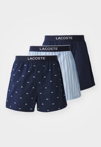 Three pairs of men's boxers: navy blue with small logo print, light blue with vertical stripes, and solid dark blue, featuring elastic waistbands.