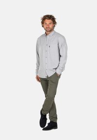 Camisa abotonada de color gris claro con mangas largas y un bolsillo en el pecho, combinada con pantalones verde oliva y zapatos negros. Textura suave.