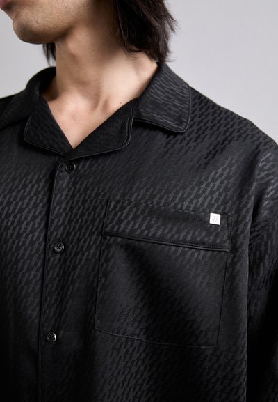 Schwarzes Hemd mit einem subtilen geometrischen Muster, aus glattem Stoff. Verfügt über einen Kragen, Knöpfe an der Vorderseite und eine aufgesetzte Tasche mit einem Etikett.