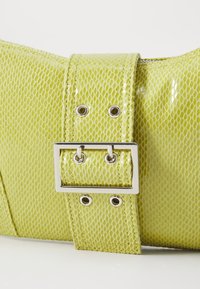 Sac à main texturé vert avec une finition brillante, présentant une grande sangle réglable avec boucle et des accents en métal argenté.
