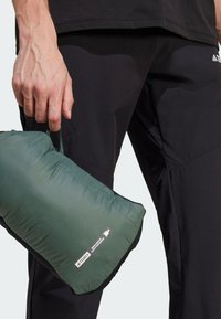 Grüner isolierter Beutel mit einem Griff, der eine glatte Textur, schwarze Akzenten und ein Logo-Etikett an der Seite aufweist, gehalten von einer Hand.