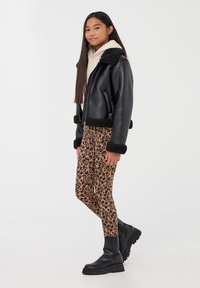 Giubbotto di pelle nera con dettagli in shearling, felpa beige e leggings con stampa leopardata in marrone e nero. Stivaletti neri chunky alla caviglia.