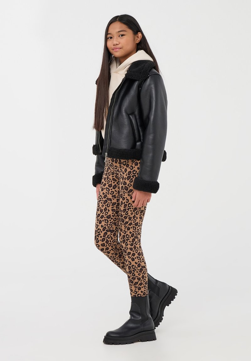 Giubbotto di pelle nera con dettagli in shearling, felpa beige e leggings con stampa leopardata in marrone e nero. Stivaletti neri chunky alla caviglia.