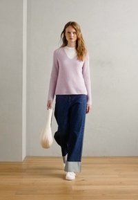 Pulover tricotat cu relexie de culoare lila deschis, asortat cu blugi din denim închis, cu picior larg și manșetă. Modelul poartă o geantă tote de culoare crem și adidași albi.