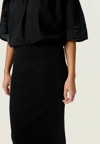 Jupe noire côtelée avec une silhouette ajustée, associée à un haut noir décontracté en tissu texturé et à manches courtes.