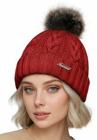 Red knitted beanie featuring a textured cable pattern, ribbed brim, and a fluffy faux fur pom-pom on top with a small logo detail.
